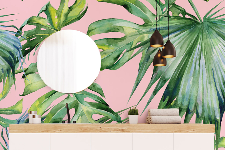 pink wallpaper with green tropical leaves on wall behind round glass mirror in bathroom