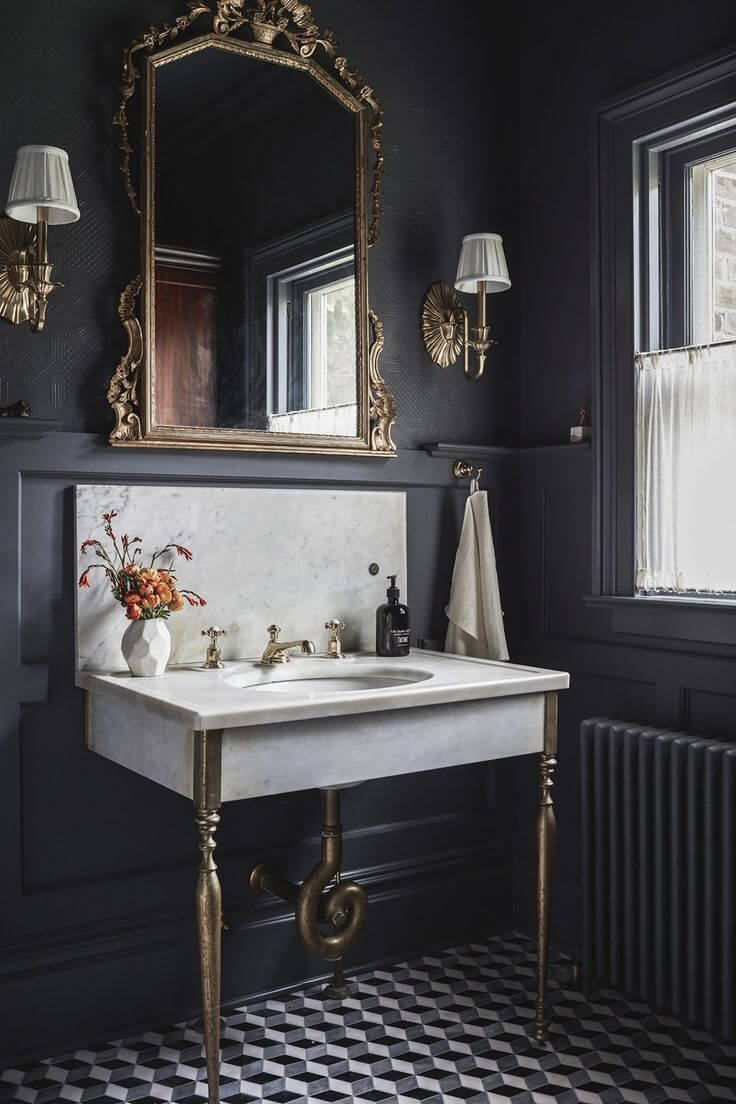 Black walls in a bathroom with a white marble sink and a gold mirror and taps