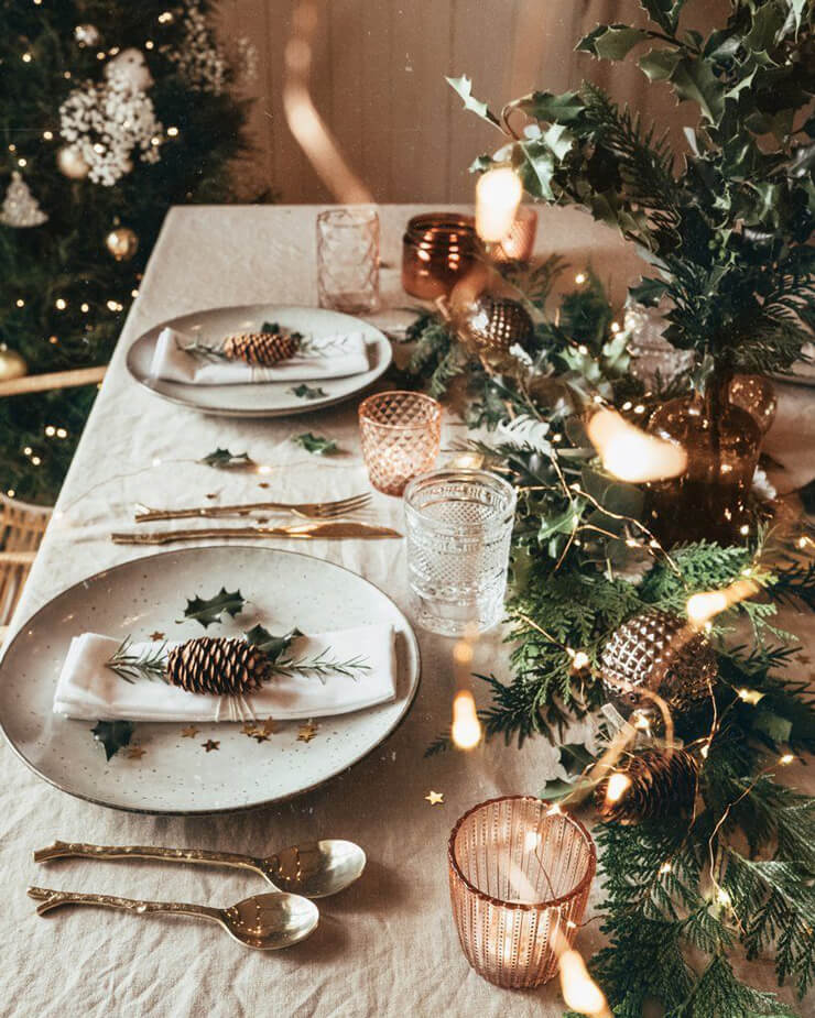 Christmas table with beige table cloth and plates with pinecones and gold cutlery 
