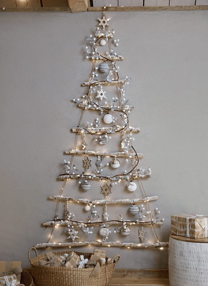 Flat wooden Christmas tree on a grey wall with light and silver baubles