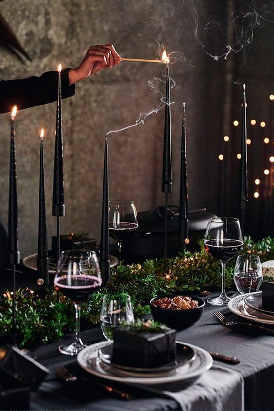 Dark dining room with a table covered in a black table cloth with white and black plates and black candles