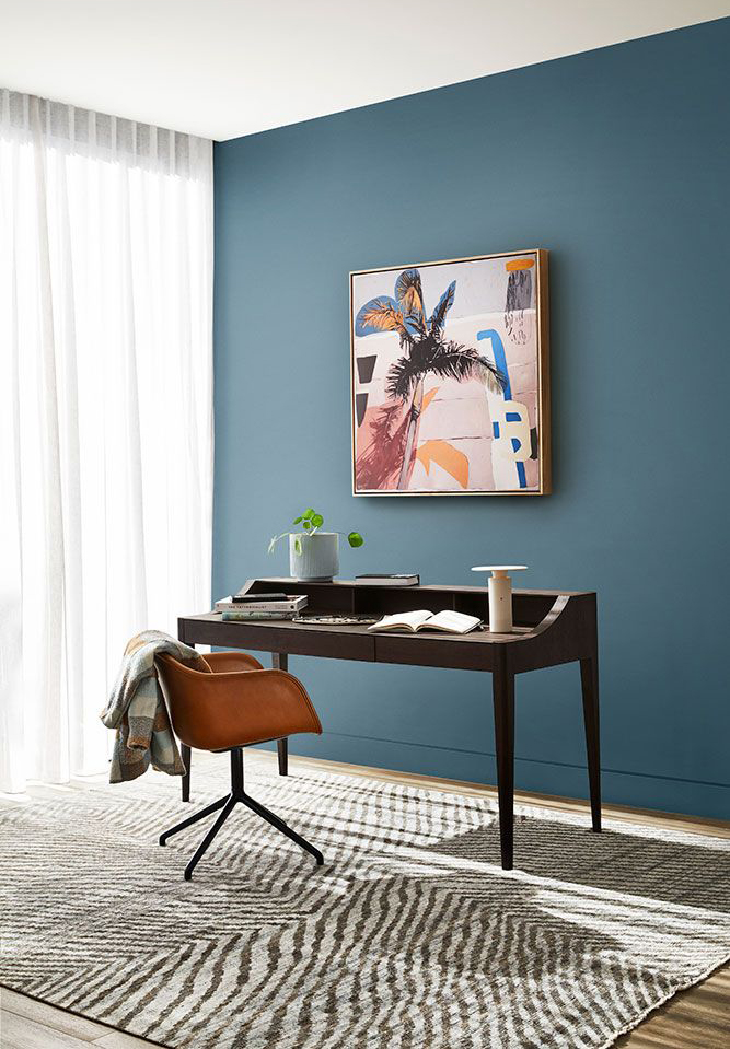 inky-blue painted walls in sleek office with wooden desk and colourful wall art