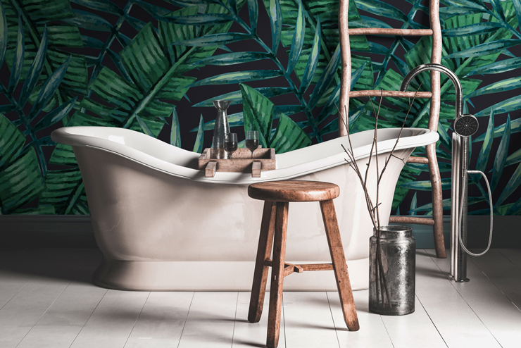 painted dark jungle leaves wallpaper in boho style bathroom with free-standing tub and wooden stool
