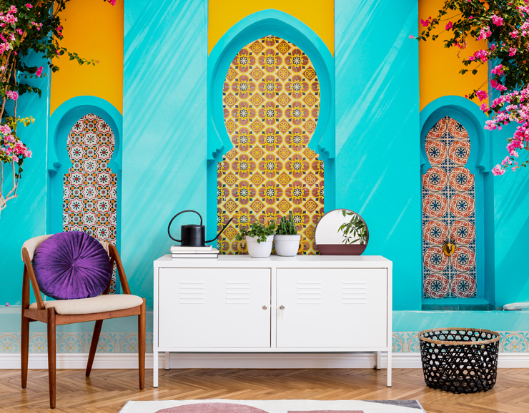 orange and blue photograph of Moroccan building with colorful tiles wallpaper in living room with white cabinet and chair with purple round cushion 