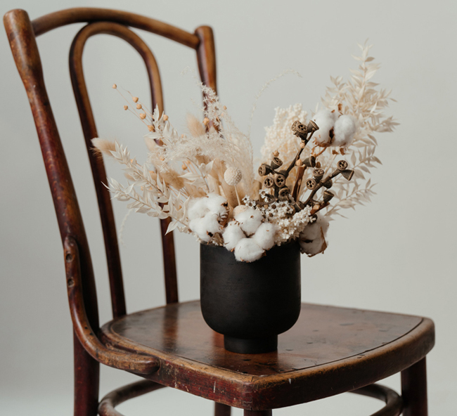 dried flowers and cotton in black vase on brown wooden chair