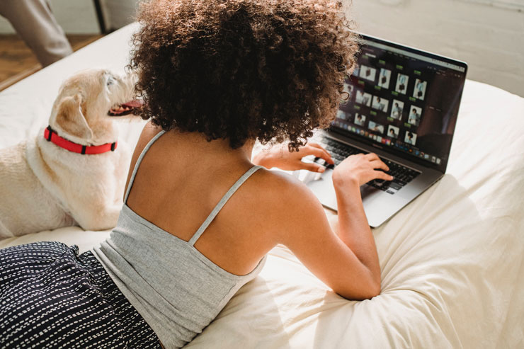 woman working on laptop in bed with dog sat next to her