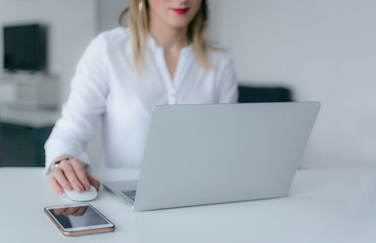 blond woman wearing a white shirt on her laptop not looking at her phone