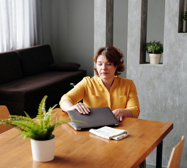 woman with yellow shirt putting away her laptop when the working day is over