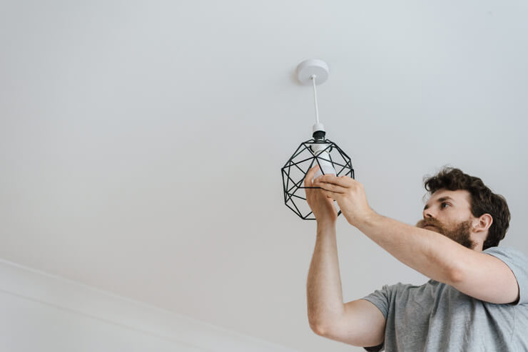 brown haired man with beard changing a ceiling bulb