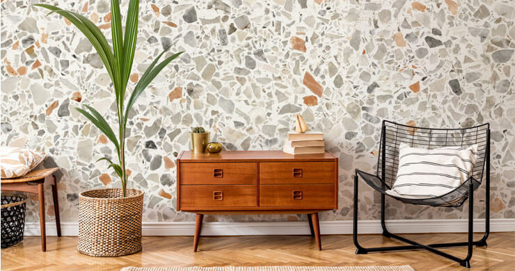 terracotta, grey and off-white terrazzo wallpaper in room with mid-century wooden drawers and green plant