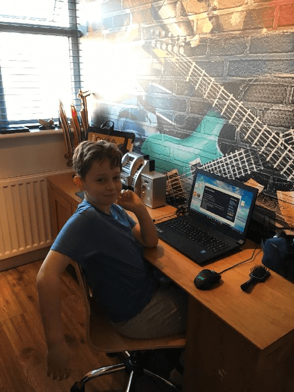 graffiti guitar wall mural behind child's desk with boy sat there with laptop