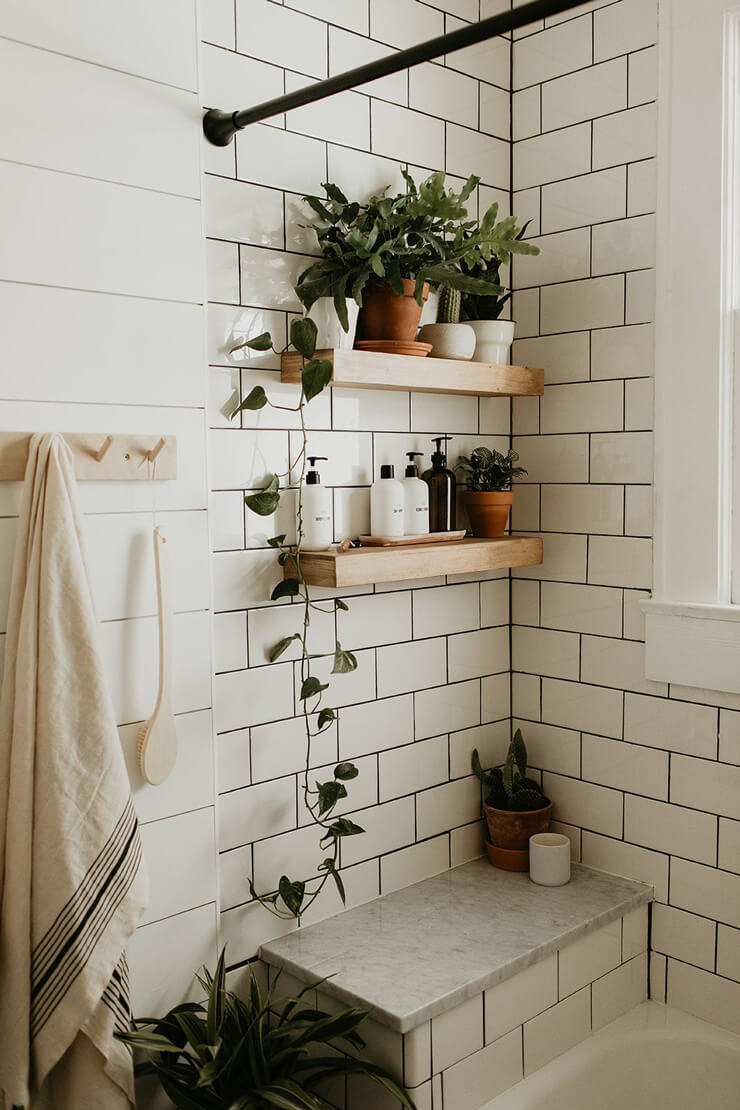 white tiled bathroom with black grouting, tropical plants and wooden and clay room accessories