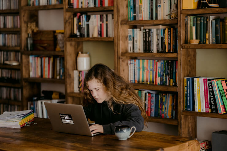 long brown haired girl with laptop with book shelves