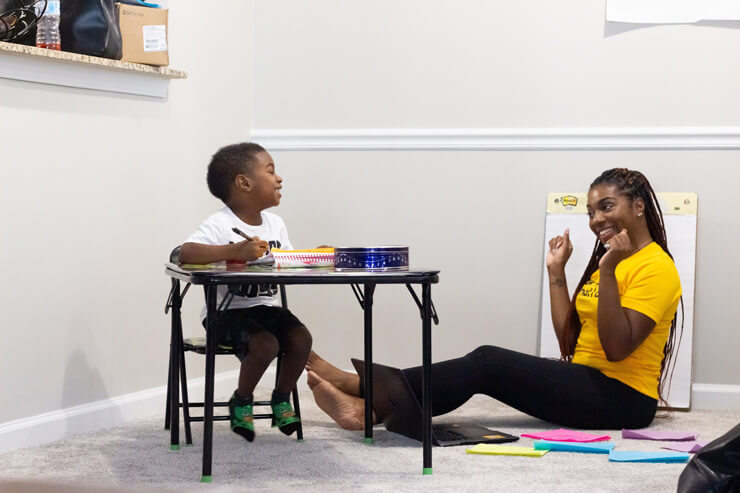 little boy sat at table with his mum who is home teaching him