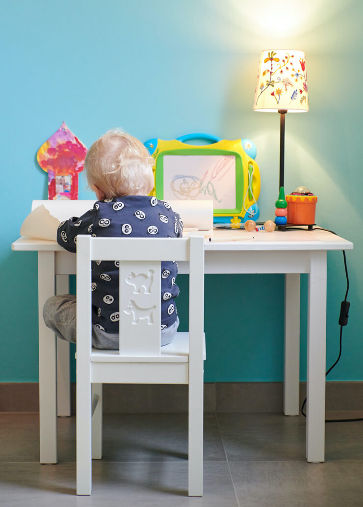 blonde haired toddler sat at white desk with flower lamp