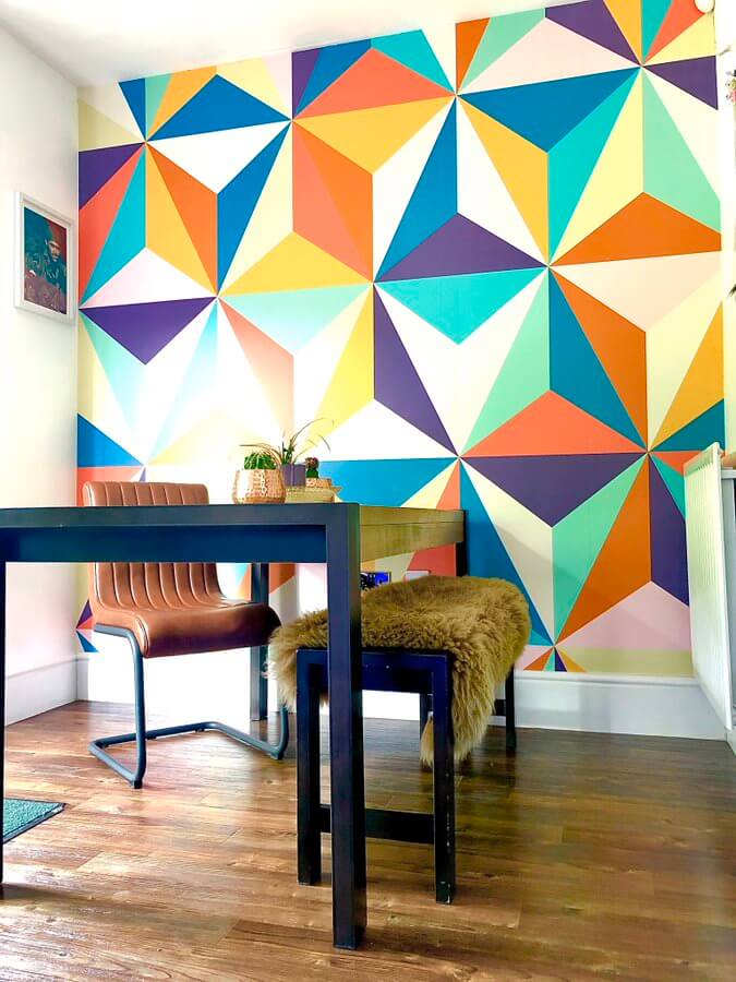 multicolored geometric triangle wallpaper in retro 70s style room with wooden desk and fur covered bench