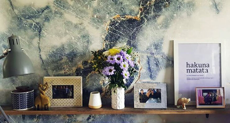 blue and white marble effect wallpaper behind floating shelves with flowers and photos