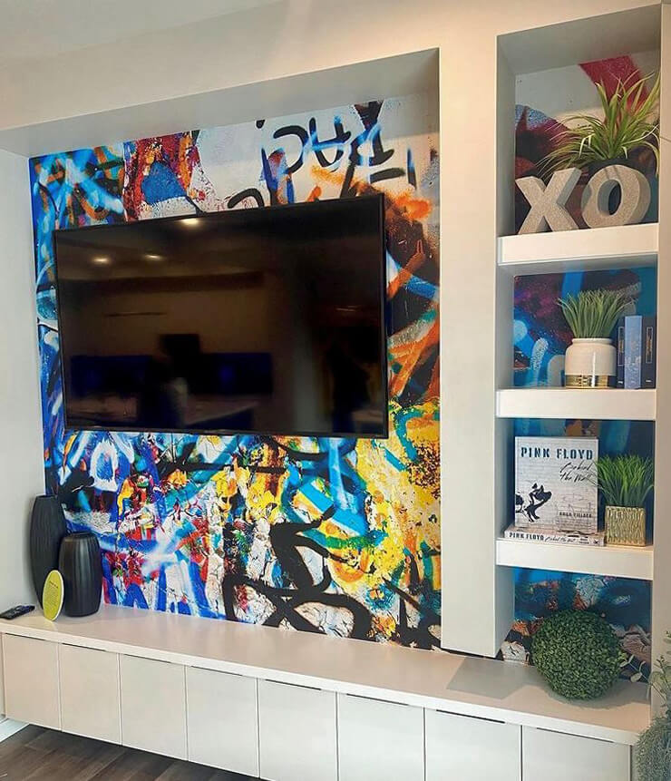mounted tv and white shelving on colourful graffiti wallpaper