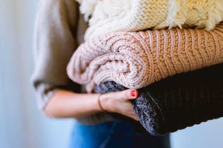 woman holding jumpers to store away and declutter and create home organization