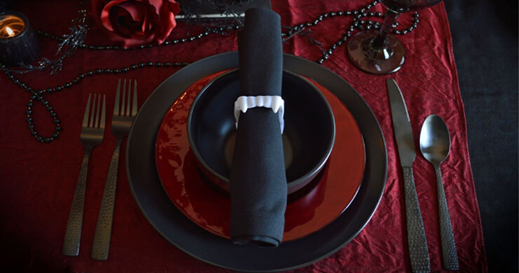 Black and red Halloween party decorations with a table setting with vampire teeth holding a black napkin