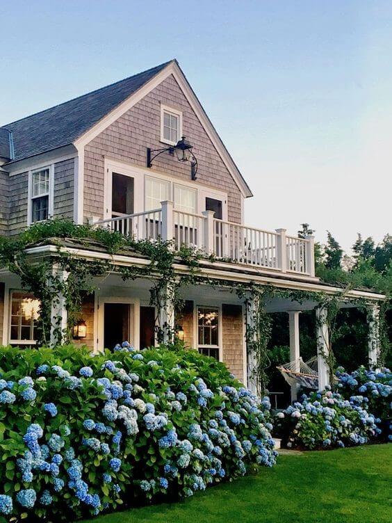 Front of a coastal granddaughter inspired house which has a white balcony and blue hydrangeas