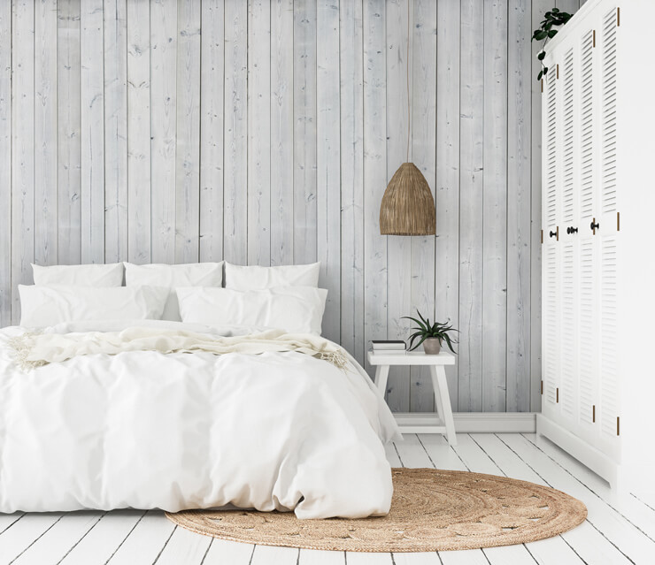 White coastal inspired bedroom with white bed sheets and a white wood panel wallpaper