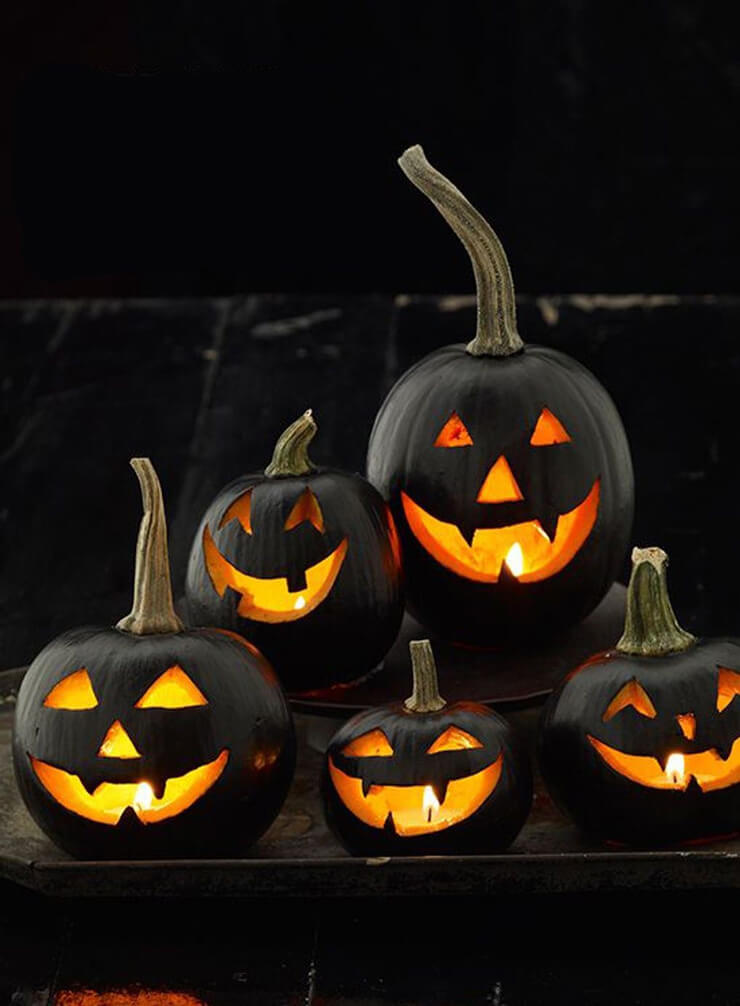 Pumpkins painted black with carved glowing faces in the dark