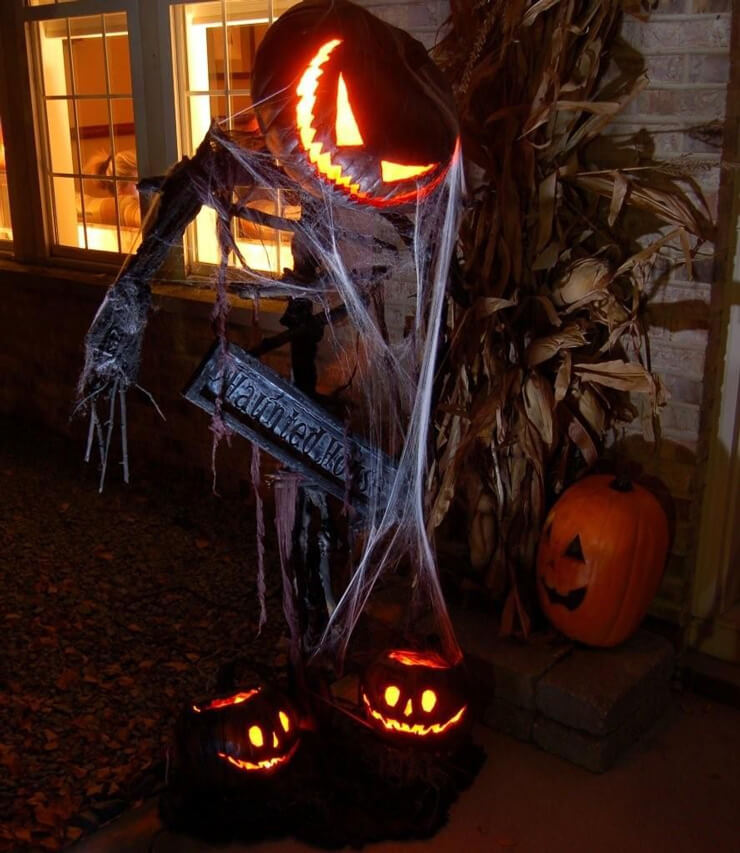 Scarecrow with a glowing pumpkin head in a dark garden with cobwebs and more carved pumpkins