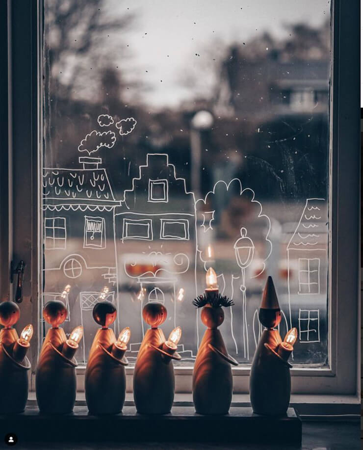 Close up on a window with a drawn Christmas village on the glass with warm white lights