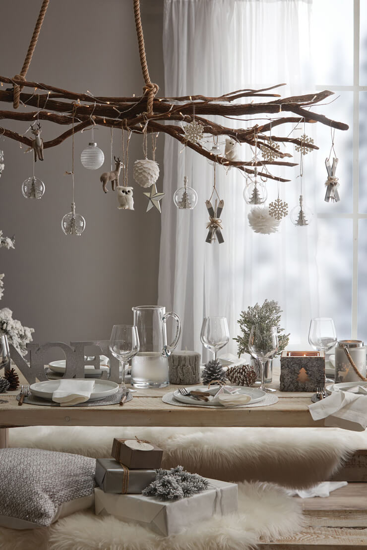 Hanging wooden Christmas decorations on branches over a wooden christmas table 
