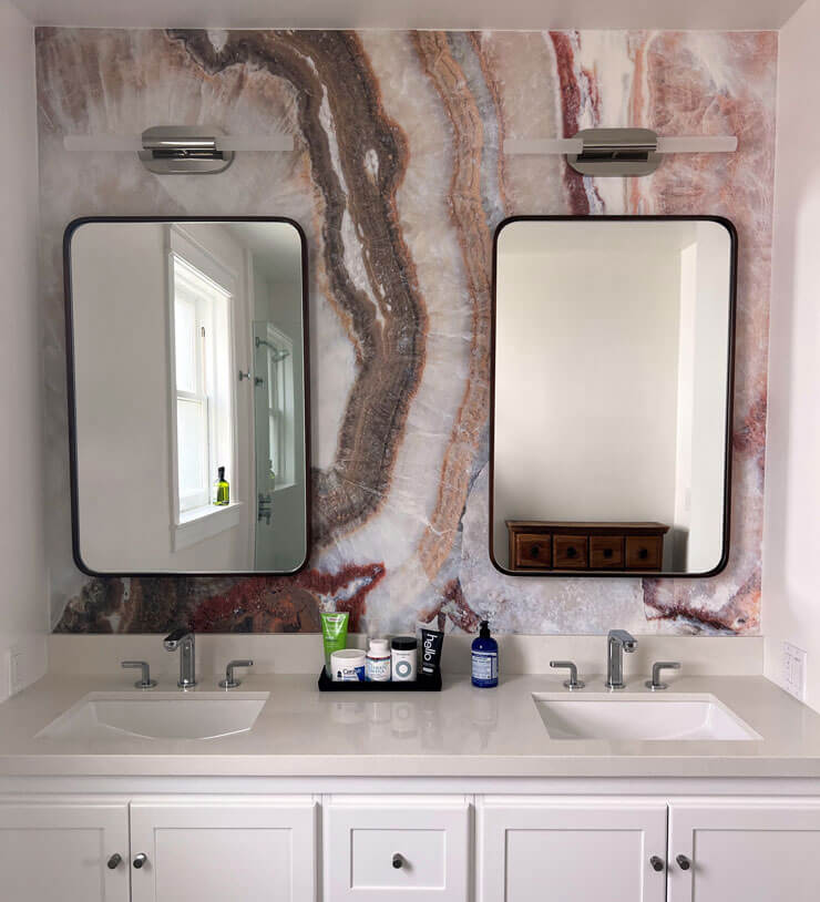 White bathroom units with a pale pink marble wall mural decorated with black framed mirrors