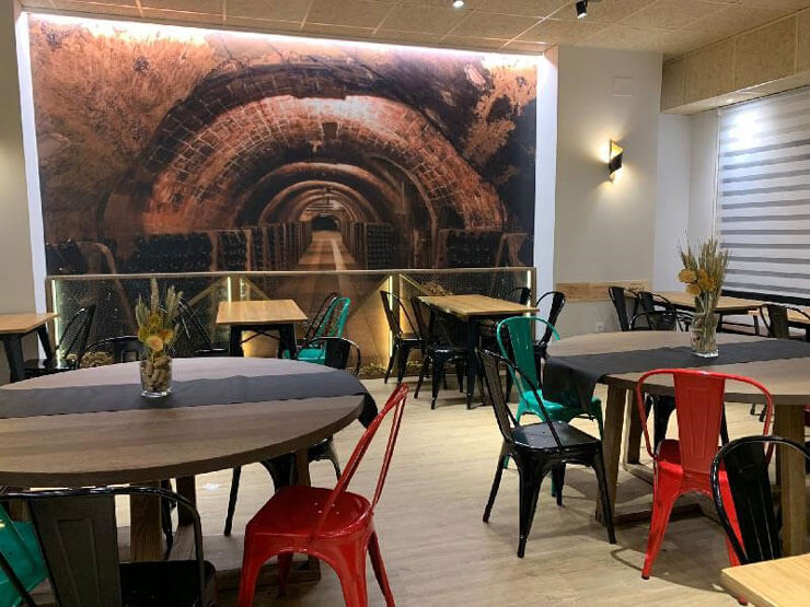 3D wine cellar wallpaper mural in a wine bar with wooden tables and green and red chairs