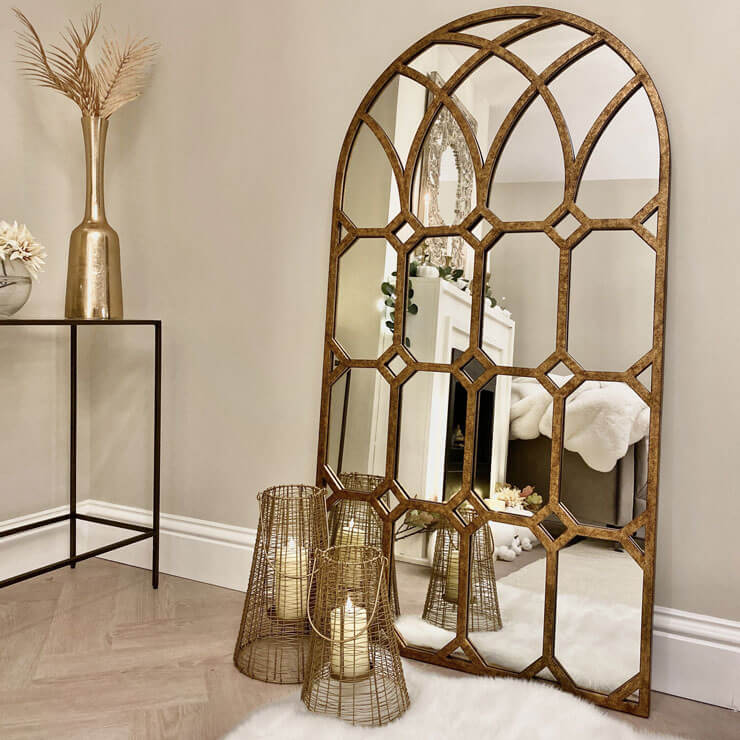 Large gold mirror in a hallway leant against a wall with golden accessories