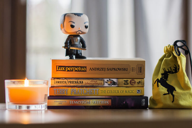 Stack of fantasy books with a figurine and a candle