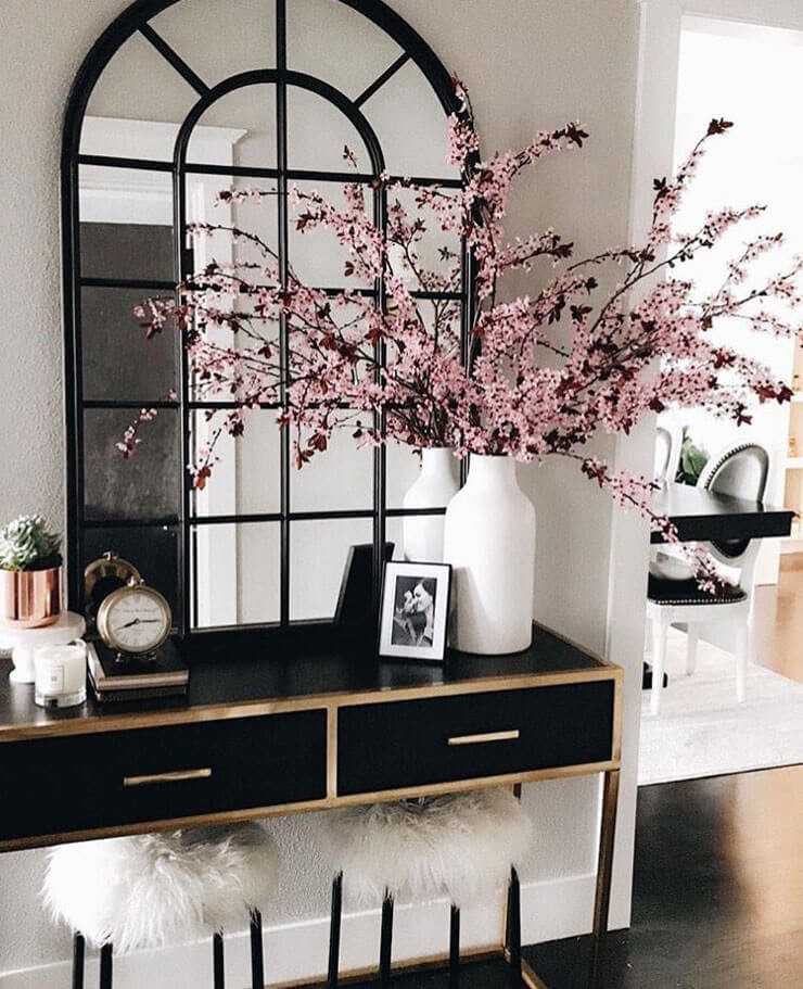 Hallway with a black and gold table with a black mirror and tall pink flowers