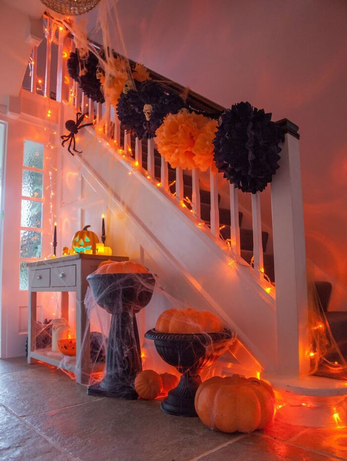 Stairs and hallway decorated with orange Halloween lights, pumpkins and pretend spider webs