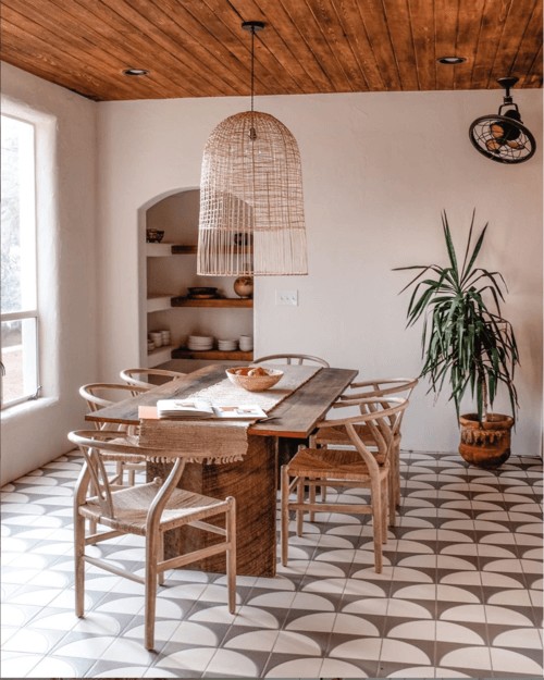 Neutral dining room with a brown geometric tile floor, wooden table and rattan chairs and light shade
