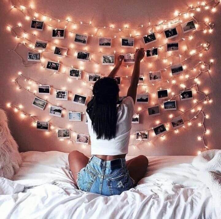 girl pinning up photo wall and fairy lights