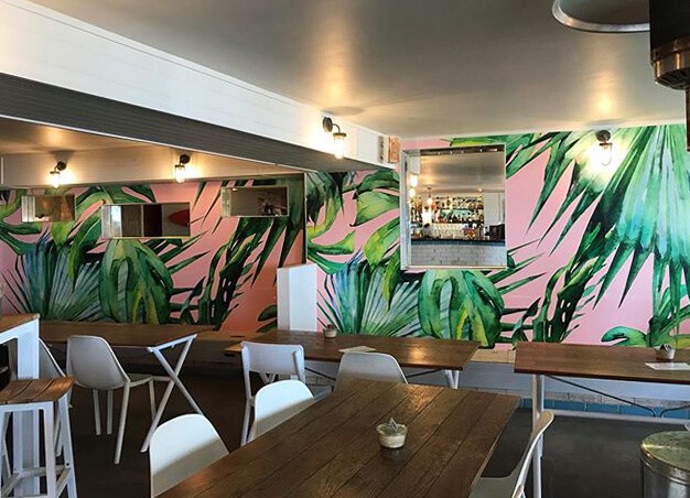 Pink and green tropical wallpaper in a cafe with dark wood tables and chairs