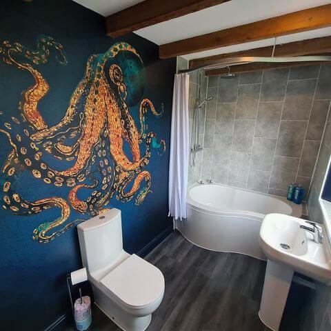 navy and gold toned octopus wallpaper in bathroom with large bath, toilet and sink