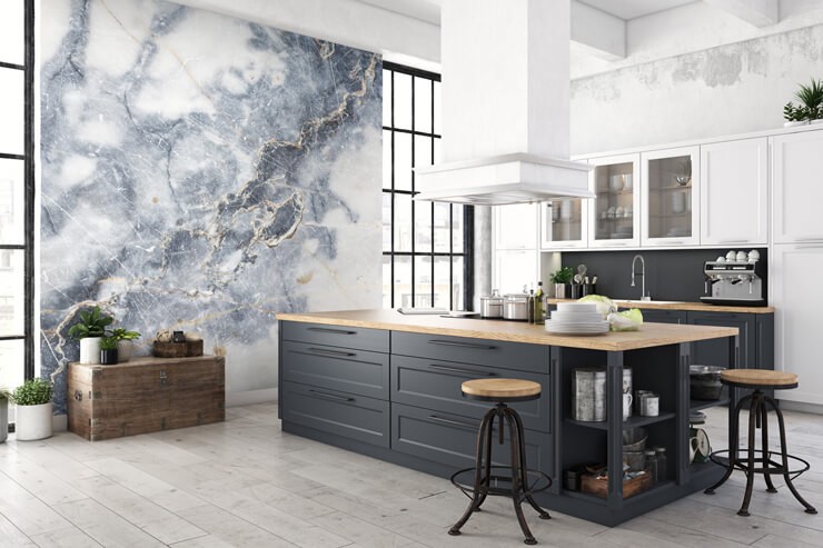 Large kitchen with a blue and white marble wallpaper with blue/grey cupboards and pine worktops