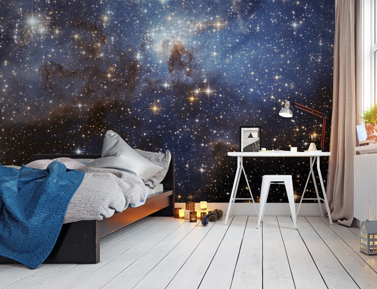 Blue starry space wallpaper in a bedroom with a white wooden floor and desk and a bed with grey and white bedsheets