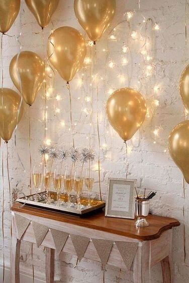White brick wall with a white wooden table and golden balloons with champagne glasses