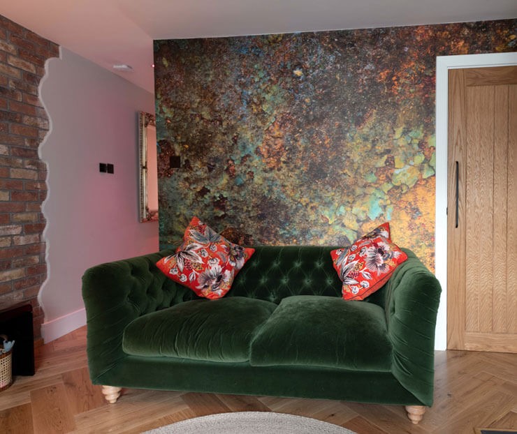 Metal effect wallpaper behind a dark green sofa with a wooden floor and exposed brick wall