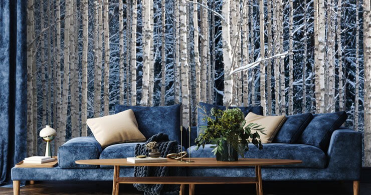 Woodland wallpaper for every season with a snowy blue birch tree wallpaper in a living room with a blue sofa and beige rug