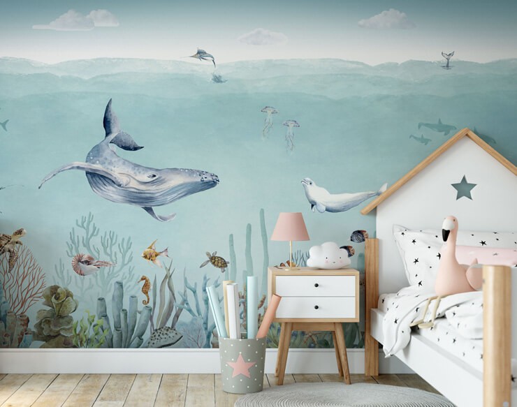 Pastel wallpaper with illustrative sea life in a child's bedroom with a wooden floor and white furniture