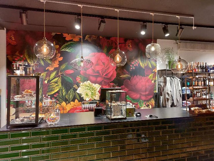 Large, dark floral wall mural behind a bar with low hanging lights and green tiles