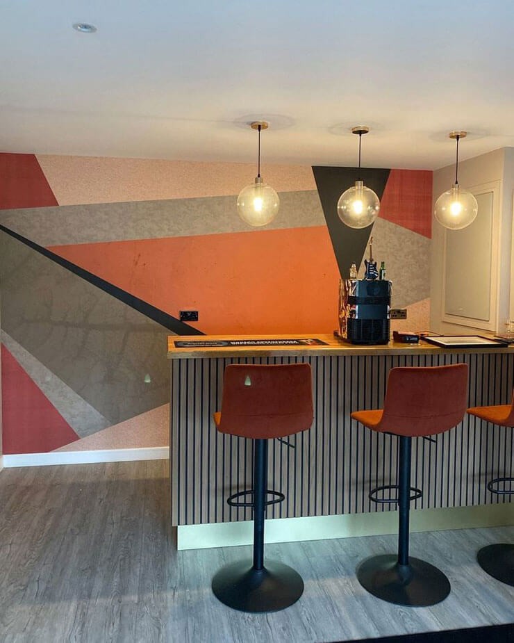 Orange and black geometric wallpaper in a home bar with orange accessories