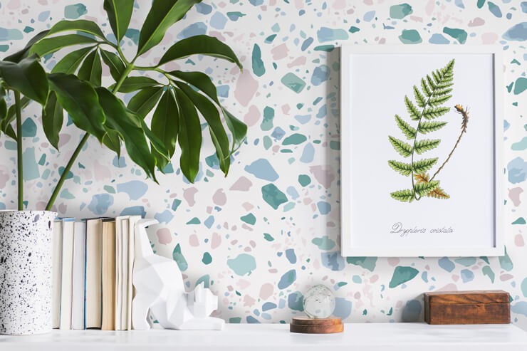 Pastel terrazzo wallpaper behind a white shelf with neutral books and white and wooden ornaments