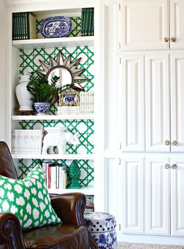 White fitted bookshelves painted with green geometic shapes in a white living room with green cushions